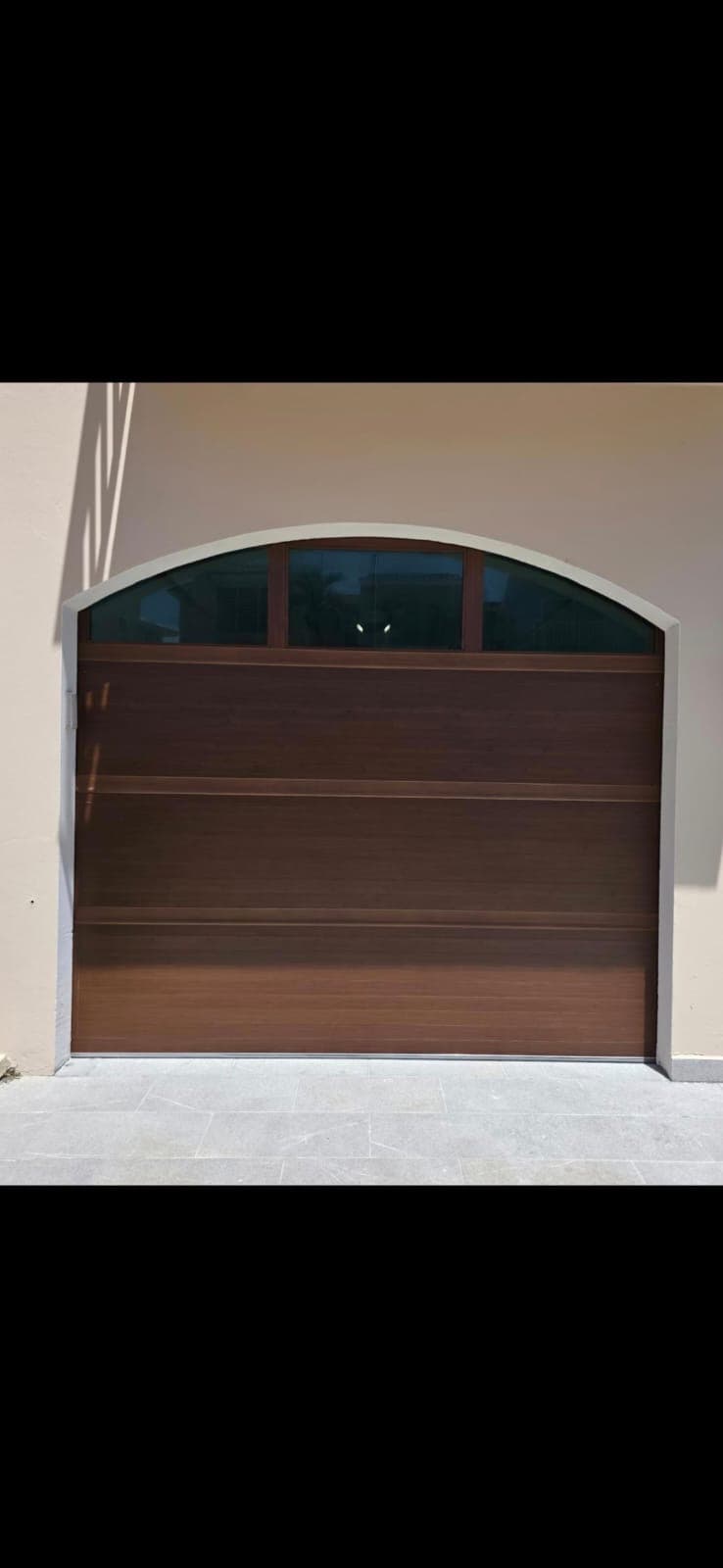 Modern dark wood-grain garage door with an arched top and three glass window panes.