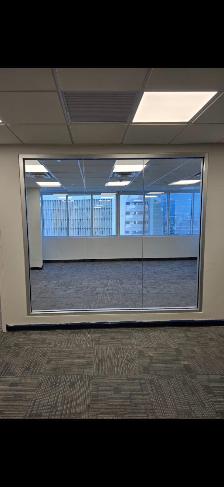 Empty office space with grey patterned carpet tiles seen through a large glass partition wall.