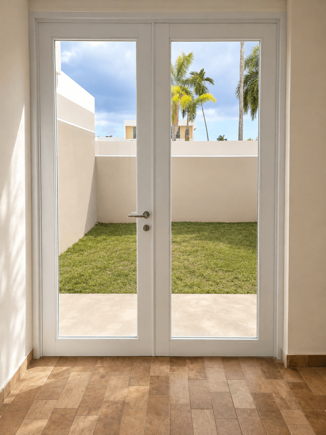 White glass French doors looking out onto a small green lawn and tropical palm trees.