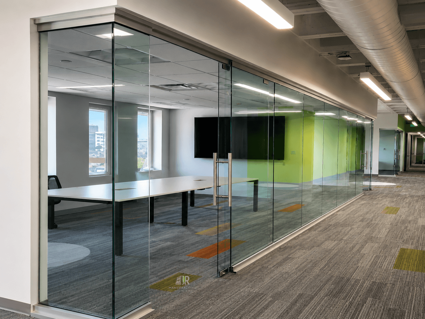 Modern office interior featuring glass-walled conference rooms, white tables, and colorful carpet tile accents.