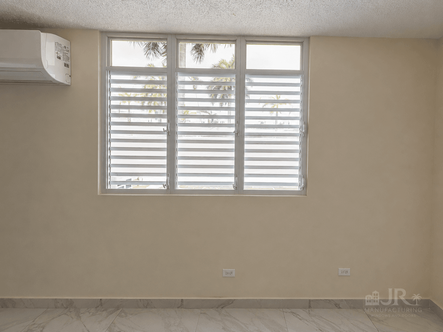 Three-paneled white jalousie window with horizontal slats overlooking palm trees in a beige room.