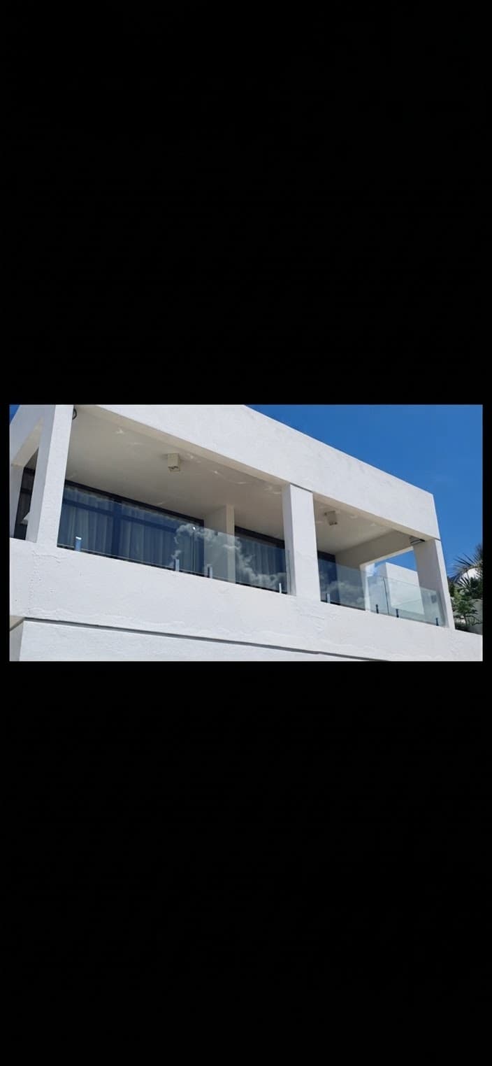 Modern white building with glass-railed balconies under a clear, bright blue sky.